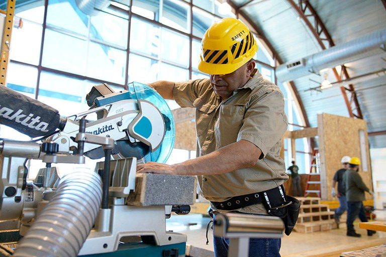 Student using a miter saw for construction of an eco-friendly home.