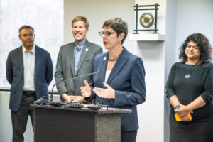 Tracy Hartzler, CNM President, standing at a podium while Mayor Keller and two others look on.